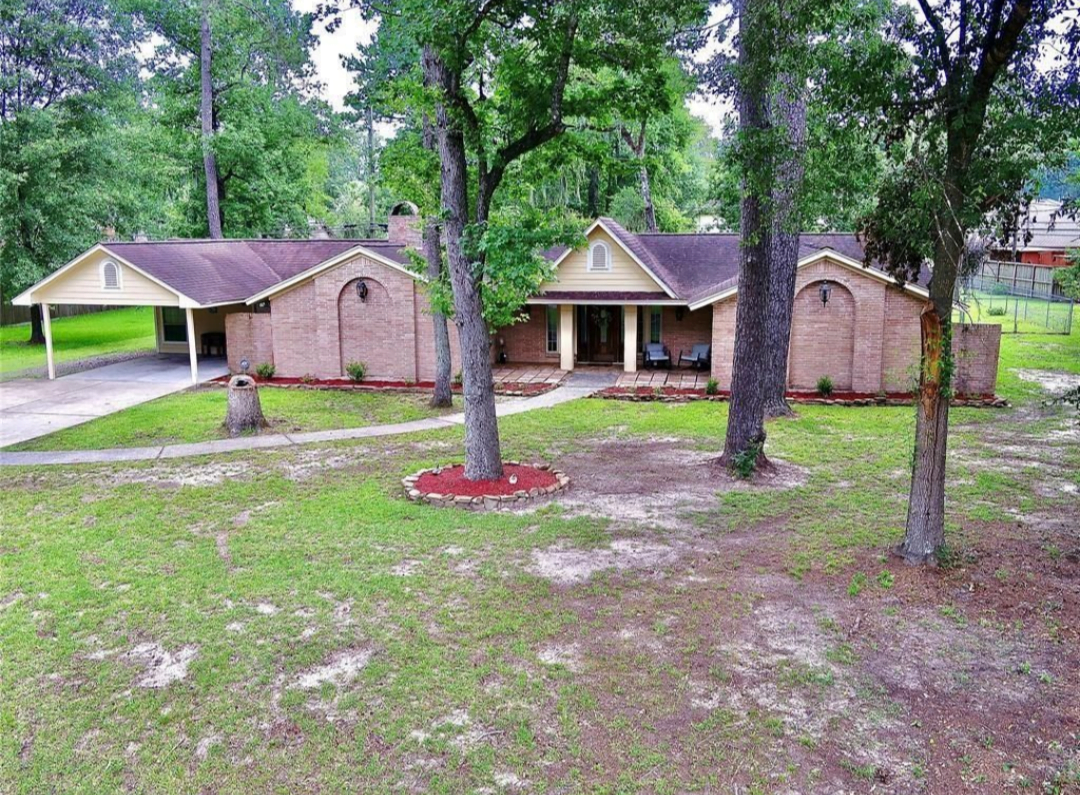 Two-story brick house with a covered porch and mature trees in a suburban neighborhood.