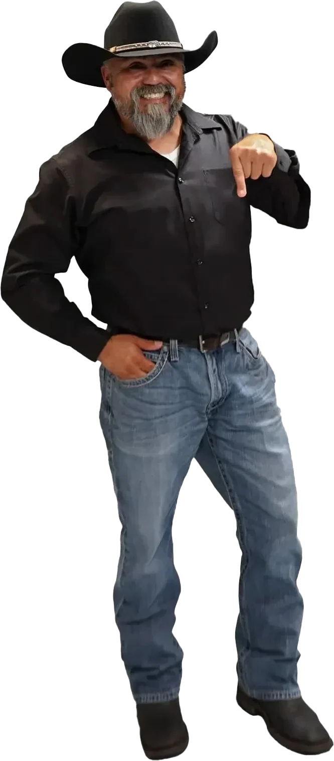 Stephen dressed in a black cowboy hat, black button-up shirt, and blue jeans. He has a gray beard and is smiling, standing in a relaxed posture. His left hand rests on his hip, while his right hand is pointing downward, emphasizing a direction or spot below him. He appears cheerful and confident, projecting a laid-back, Western-style look.