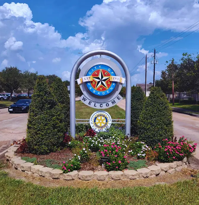 Welcome sign of the City of Pasadena, Texas, surrounded by neatly trimmed bushes, vibrant pink and white flowers, and a clear blue sky in the background, adding a welcoming and community-focused feel to the area.